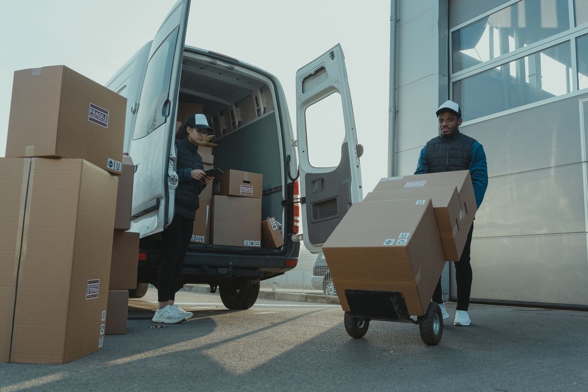 Two delivery workers unloading cardboard boxes from an open white van using a dolly