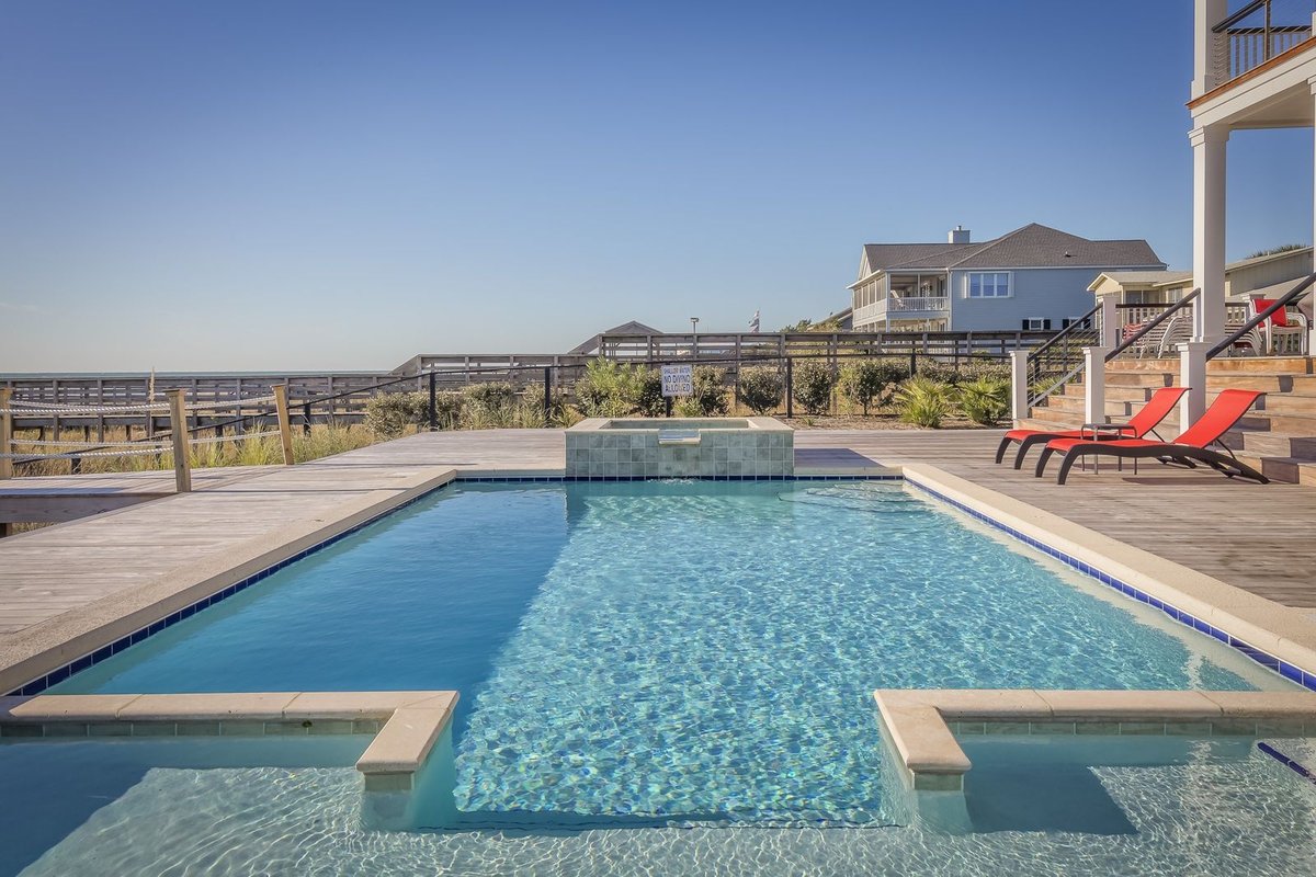 Swimming pool with a small raised spa, timber deck and red sun loungers