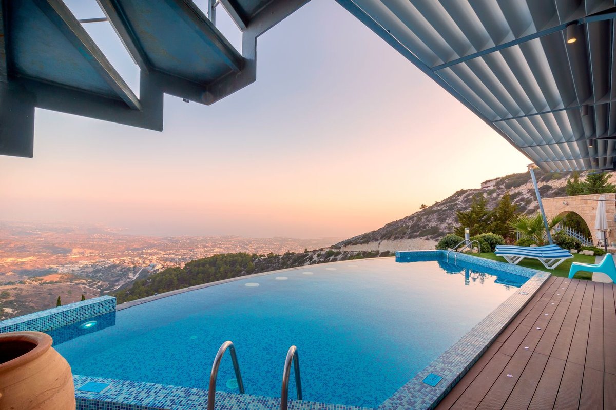 Infinity pool under the edge of a louvred shade roof at sunset, with loungers on the deck